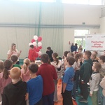Tłum dzieci widzianych od tyłu_ przed nimi po prawej kobieta w białej bluzce gestykulująca rękoma..jpg
