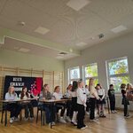 Grupa uczniów siedząca w ławkach_  część uczniów stoi przed ławkami..jpg