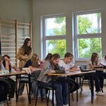 Grupa uczniów siedząca w ławkach_  jedna uczennica stoi z tyłu..jpg