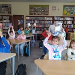 Uczniowie siedza w ławce i podnosza wypozyczone ksiązki.jpg