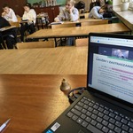 Widok ekranu w lapotopie_ w tle uczniowie siedzący w ławkach w klasie..jpg