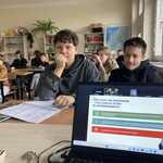 Widok ekranu w lapotopie_ w tle uczniowie siedzący w ławkach w szkolnej klasie..jpg