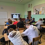 Widok monitora z wyświetlanym tekstem_ przed nim siedzący tyłem uczniowie w ławkach..jpg