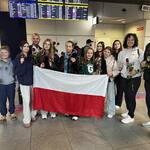 Gruap młodzieży i osób dorosłych stoi z flagą Polski oraz różami..jpg