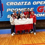 Grupa sportowców ubrana w barwy biało-czerwone pozuje na tle niebieskiego baneru  z napisami.jpg