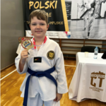 Chłopiec ubrany w stój karate pozuje z medalem w ręku.PNG
