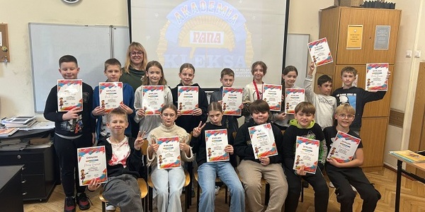 Grupa uczniów pozuje do zdjęcia w klasie. Wszyscy trzymają klorowe dyplomy w rękach..jpeg