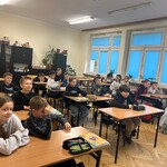 Grupa uczniów siedzących w  ławkach szkolnych  pozuje do zdjęcia w klasie..jpeg