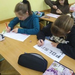 Grupa uczniów maluje karty pracy w klasie.jpg