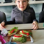 Dziewczynka siedzi przy stole z trzema kanapkami z warzywami..jpg