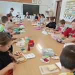 Grupa dzieci siedzi przy dużym stole w klasie i przygotowuje kanapki z produktów spożywczych.jpg