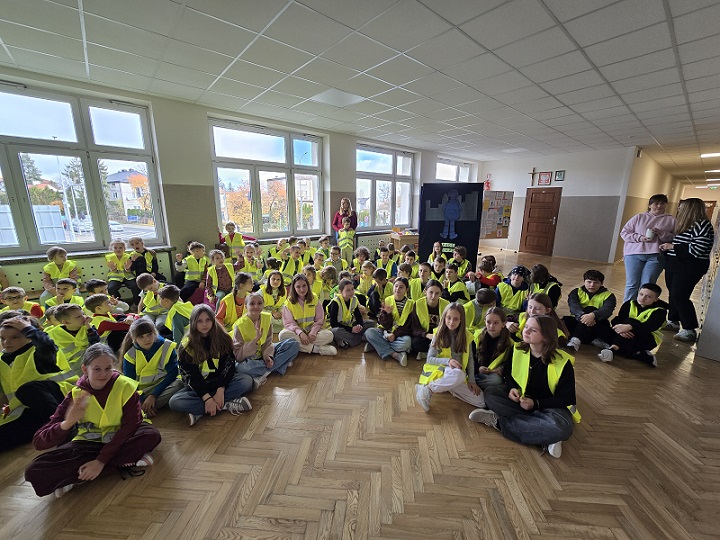 duża grupa dzieci siedzi na podłodze w odblskowych kamizelkach.jpg