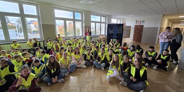 duża grupa dzieci siedzi na podłodze w odblskowych kamizelkach.jpg