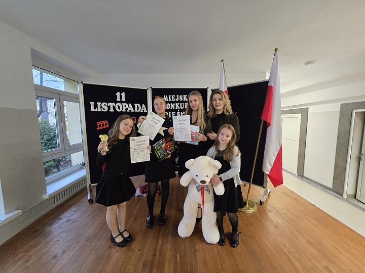 Cztery uczennice i nauczycielka stoją z nagrodami przy fladze polskiej i talicy z napisami patriotycznymi.jpg