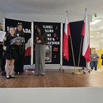 Uczennica stoi na podium z nagrodą_ obok przez mikrofon przemawia kobieta prowadząca konkurs.jpg