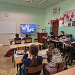 Grupa uczniów siedzi w ławkach w klasie i ogląda film na monitorze.jpg