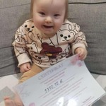 Małe niemowlę siedzi na kanapie z dyplomem i uśmiecha się do zdjęcia.jpg