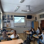 Grupa uczniów siedzi w ławkach klasowych i ogląda prezentację na ekranie..jpg