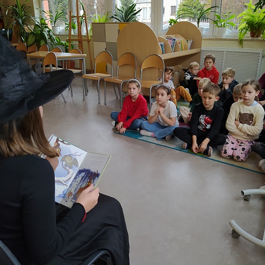 Dzieci siedzą na dywanie_ uczennica ubrana na czarno czyta dzieciom.jpg