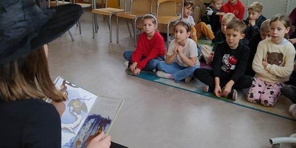Dzieci siedzą na dywanie_ uczennica ubrana na czarno czyta dzieciom.jpg