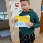 Chłopiec w zielonej bluzie z kapturem trzyma w ręku żółto-niebieski rysunek.jpg