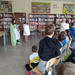 Uczniowie siedzą w czytelni_ przed nimi stoją dziewczynki w stroju wiosny.jpg