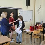 Dwie nauczycielki wręczają nagrodę uczennicy w sali lekcyjnej.jpg