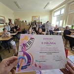 Zdjecie dyplomu za zajęcie 2 miejsca na tle uczniów siedzących w sali.jpg