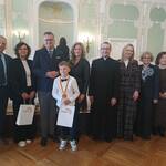 Grupa osób ubranych elegancko pozuje do zdjęcia w barokowej sali..jpg