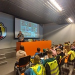 Pisarz prezentuje swoje książki stojąc przed dziećmi.jpg