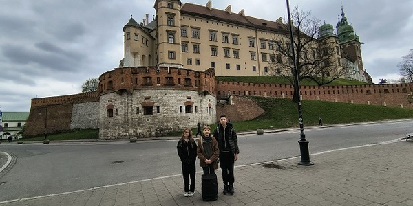 Troje uczniów stoi przed zamkiem na Wawelu.jpg