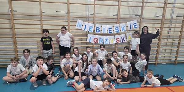 Grupa dzieci ubrana na sportowo pozuje przy drabinkach na hali sportowej.jpg