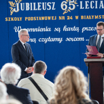 Dyrektos szkoły i gość na scenie przy mówniecy_ w tle napisy na niebieskim płótnie.jpg