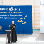 Osoba duchowna przemawia na scenie przy mównicy_ w tle flaga Polski i napisy na niebeiskim płótnie.jpg