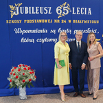 Pan dyrektor pozuje z 2  elegancko ubranymi paniami na tle napisów na niebieskim płótnie.jpg