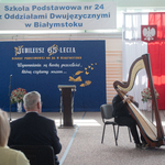 uczeń grający na wilonczeli na tle flagi biało-czerwonej i napisów na niebieskim tle.jpg