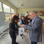 Mężczyzna wręcza torebkę z prezentem kobiecie_ w tle inne osoby..jpg