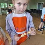 Dziewczynka w czerwonym fartuszku trzyma szaszłyka z owocami.jpg