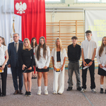 Grupa uczennic i uczniów elegancko ubranych pozuje do zdjęcia  z dyrektorem i kobieta ubraną w czerwona sukienkę.jpg