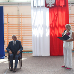 Mężczyzna siedzi w fotelu i patrzy na elegancko ubraną kobietę mówiącą do mikrofonu.jpg