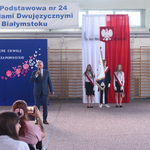 Pan dyrektor przmawia do mikrofonu na hali sportowej_ w tle flaga Polski i godło oraz poczet..jpg