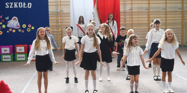 Grupa dzieci tańczy_ w  tle napis Witaj szkoło i flaga polskia z godłem..jpg