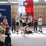 Grupa dzieci tańczy_ w  tle napis Wiatj szkoło i flaga polskia z godłem.jpg