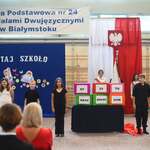 Grupa uczniów ubranych na czarno stoi przy kolorowych pudełkach z czarnym napisem.jpg