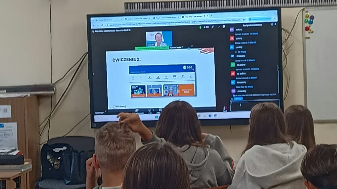 Uczniowie w ławkach obserwują monitor i prezentowane plansze z zadaniami.jpg