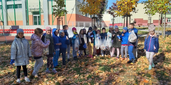 Dzieci stojące z workami pełnymi śmieci wśród liści jesiennych.