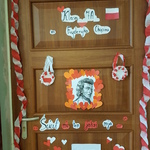 Brązowe drzwi klasy ozdobione plakatem z podobizną osoby oraz napisem.