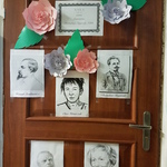 Brązowe drzwi klasy ozdobione plakami z podobizną osób oraz napisem.