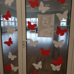 Szklane drzwi klasy ozdobione plakatem z podobizną osoby oraz biało-czerwonymi motylami
