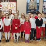 Uczniowie klasy ubrani w stroje biało-czerwone stoja przy tablicy z wystawą.